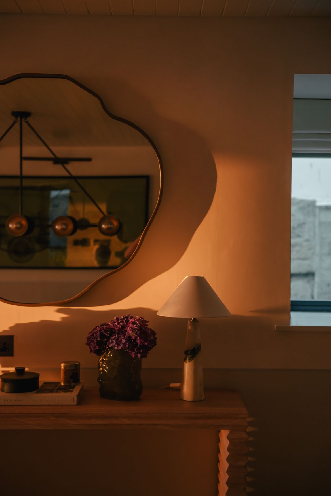 Sculptural mirror above a console in evening light
